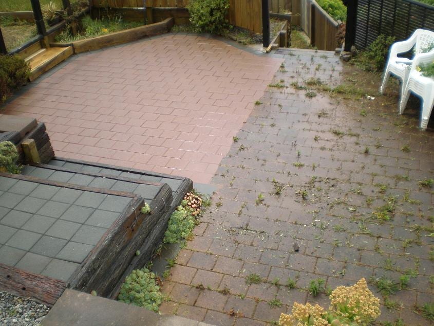 Wellington paver patio mid-clean, half-cleaned terracotta paver patio with the clean half showing rich orange tone and the uncleaned half still grey with weeds in the joints